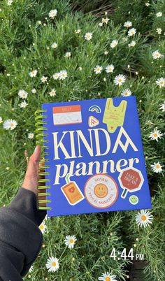 a person holding up a kinda planner in front of some daisies and flowers