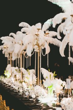 a long table topped with lots of white flowers and feathers on top of each other