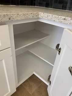 an open cabinet in a kitchen with marble counter tops and white cupboards on both sides