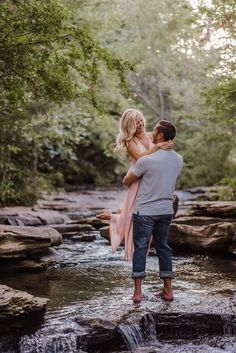 a man and woman are standing on rocks in the middle of a stream while holding each other