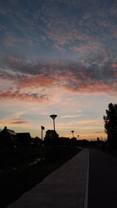 the sun is setting behind some clouds in the sky over a street and lampposts