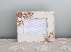 a white frame with seashells on it sitting on a lace doily next to a wall