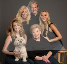 an older woman and two younger women with a dog pose for a family photo in front of a gray background