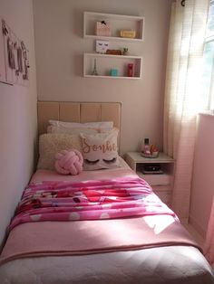 a bed with pink sheets and pillows in a bedroom next to a wall mounted shelf