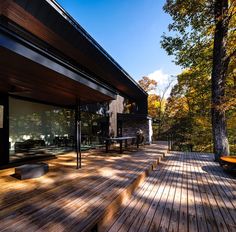 a wooden deck in front of a house with lots of windows and trees around it