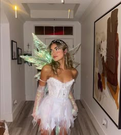 a woman dressed as tinkerbell standing in a hallway next to a painting on the wall