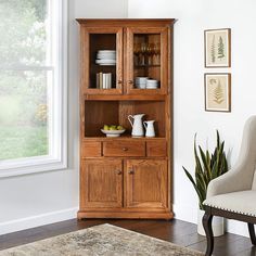 a wooden china cabinet with glass doors in a white living room next to a window