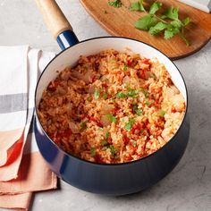 a pot filled with rice and vegetables next to a cutting board on top of a table