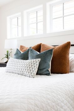 a bed with two pillows on top of it and three windows above the headboard