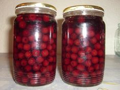 two jars filled with red berries sitting on top of a table