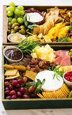 an assortment of cheeses, crackers, grapes and nuts in a wooden box