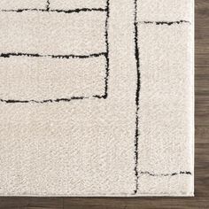 a white rug with black lines on the top and bottom, in front of a wooden floor