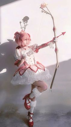 a woman dressed in white holding a bow and arrow with her right hand, while standing next to a shadow wall