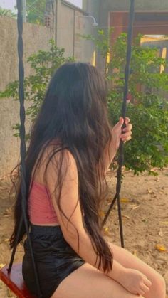 a young woman sitting on a swing in the sand with her long hair blowing back