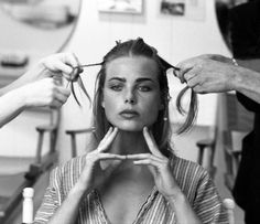 a black and white photo of a woman getting her hair styled by another woman with scissors