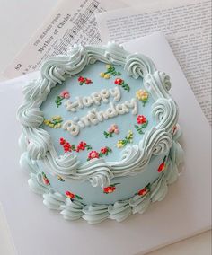 a blue frosted birthday cake sitting on top of a white table next to an open book