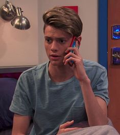 a young man talking on a cell phone while sitting in bed with his hand up to his ear