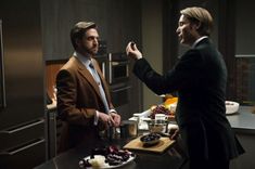 two men standing in a kitchen with food on the counter and one man is eating