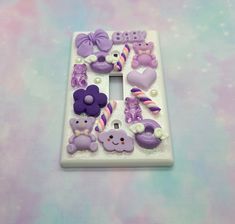 a white light switch plate covered in purple and pink decorations on top of a pastel background