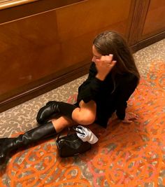 a woman sitting on the floor with her legs crossed wearing black boots and knee high socks