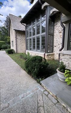 a stone house with large windows and plants in the front yard on a sunny day