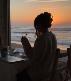 a woman sitting at a table in front of the ocean looking out onto the beach