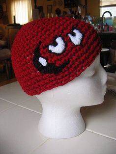 a crocheted red hat with white eyes on top of a mannequin head