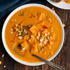 two bowls filled with soup on top of a wooden table next to silver spoons