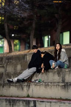 three young people sitting on the edge of steps in front of a building at night