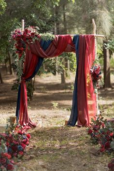 an outdoor ceremony with red and blue draping, flowers and greenery on the altar