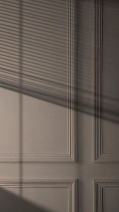 the shadow of a door handle is cast on a wall with white paint and wood slats