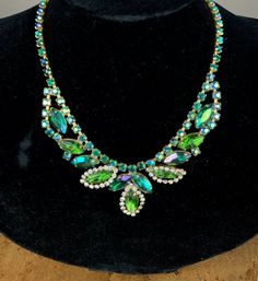 Gorgeous and brilliant midcentury necklace with gold tone base. Features bold green marquise rhinestones, some encircled by small white rounds, combined with iridescent blue-green rounds. Finding is a simple hook. A seasoned jewelry dealer friend identified these for me as pieces from the iconic Juliana D & E line.   Length is 14 1/2" not including hook. Necklace weighs 1 ounce. In excellent condition. I did a preliminary cleaning but probably could use a more skilled one. Green Jeweled Crystal Rhinestone Necklace, Green Jeweled Rhinestone Crystal Necklace, Vintage Oval Rhinestone Jewelry, Vintage Green Crystal Jewelry, Vintage Green Jeweled Jewelry, Green Rhinestone Costume Jewelry, Vintage Green Necklace For Evening, Vintage Green Necklaces For Evening, Vintage Oval Jeweled Necklaces