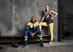 a man and woman sitting on a bench in front of a gray wall, posing for the camera