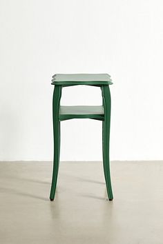 a small green table sitting on top of a cement floor next to a white wall