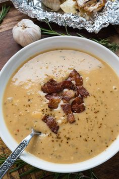 a white bowl filled with soup on top of a wooden table next to garlic and bread