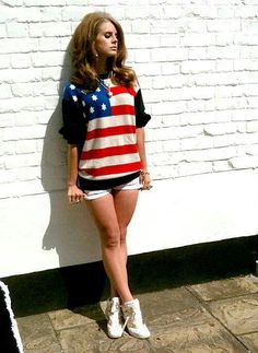 a woman standing next to a white brick wall wearing shorts and an american flag sweater