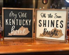 two signs are sitting on top of a bar, one is saying my dear kentucky and the other says shine bright