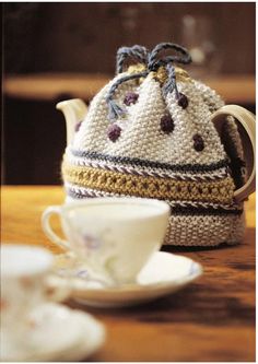 a crocheted tea cosy with a cup and saucer next to it