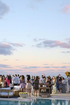 a group of people standing next to a swimming pool at sunset or dawn with clouds in the sky