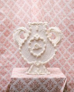 a white vase sitting on top of a pink and white tablecloth covered box with a pattern