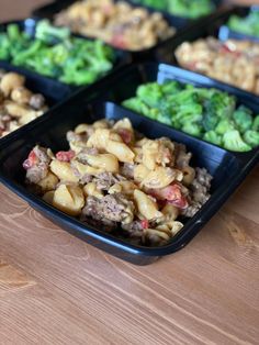 four black trays filled with food on top of a wooden table next to broccoli