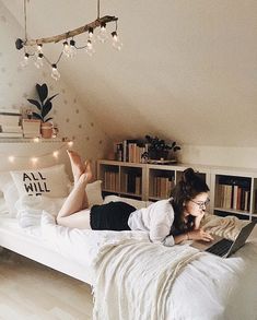 a woman is laying on her bed with a laptop in front of her and lights hanging from the ceiling