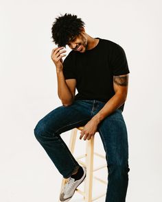 a man sitting on top of a wooden stool holding a cell phone to his ear