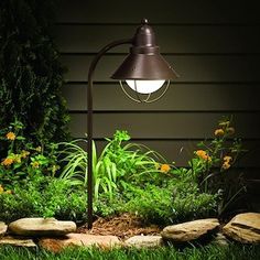 a lamp is lit up in the grass near some rocks and plants on the ground