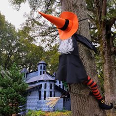 a scarecrow doll hanging from a tree in front of a blue house with an orange hat and striped socks