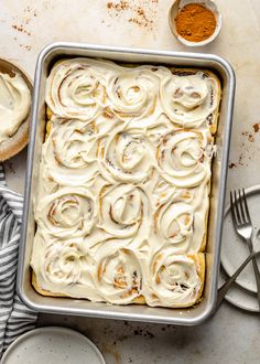 a baking pan filled with cinnamon rolls next to some plates and utensils