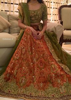 a woman in an orange and green lehenga sitting on a couch