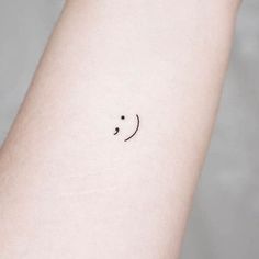 a small smiley face tattoo on the left inner arm, with black dots around it