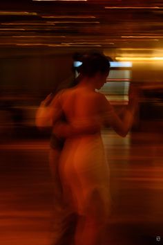 blurry photograph of two women dancing in the street at night, one woman is wearing a white dress