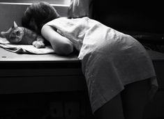 a woman laying her head on a cat's back in front of a window